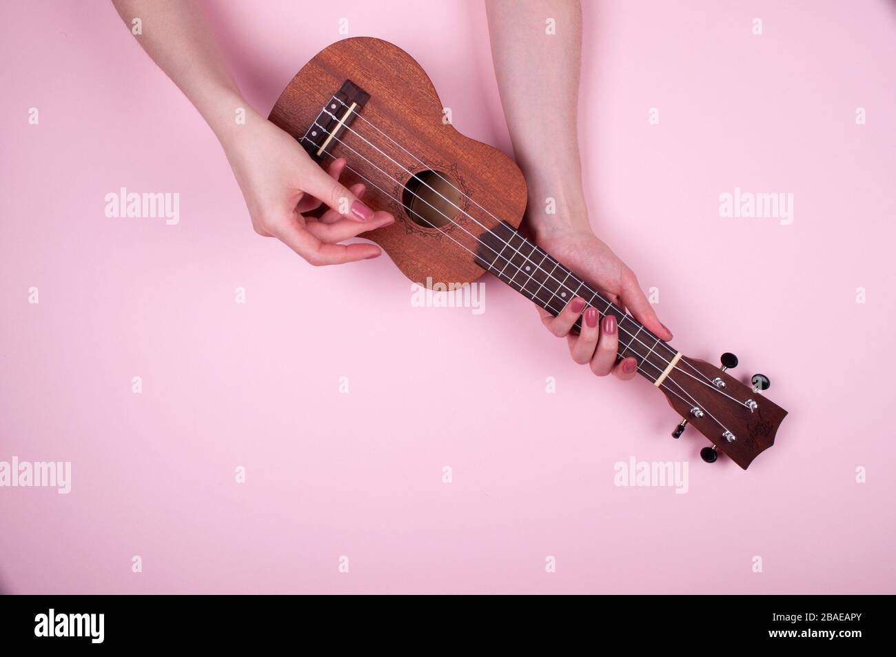 Frau Hände mit pinkfarbener Maniküre, die wenig Wodden Ukulele auf pinkfarbenem Hintergrund hält. Feines Musikerbild. Stockfoto