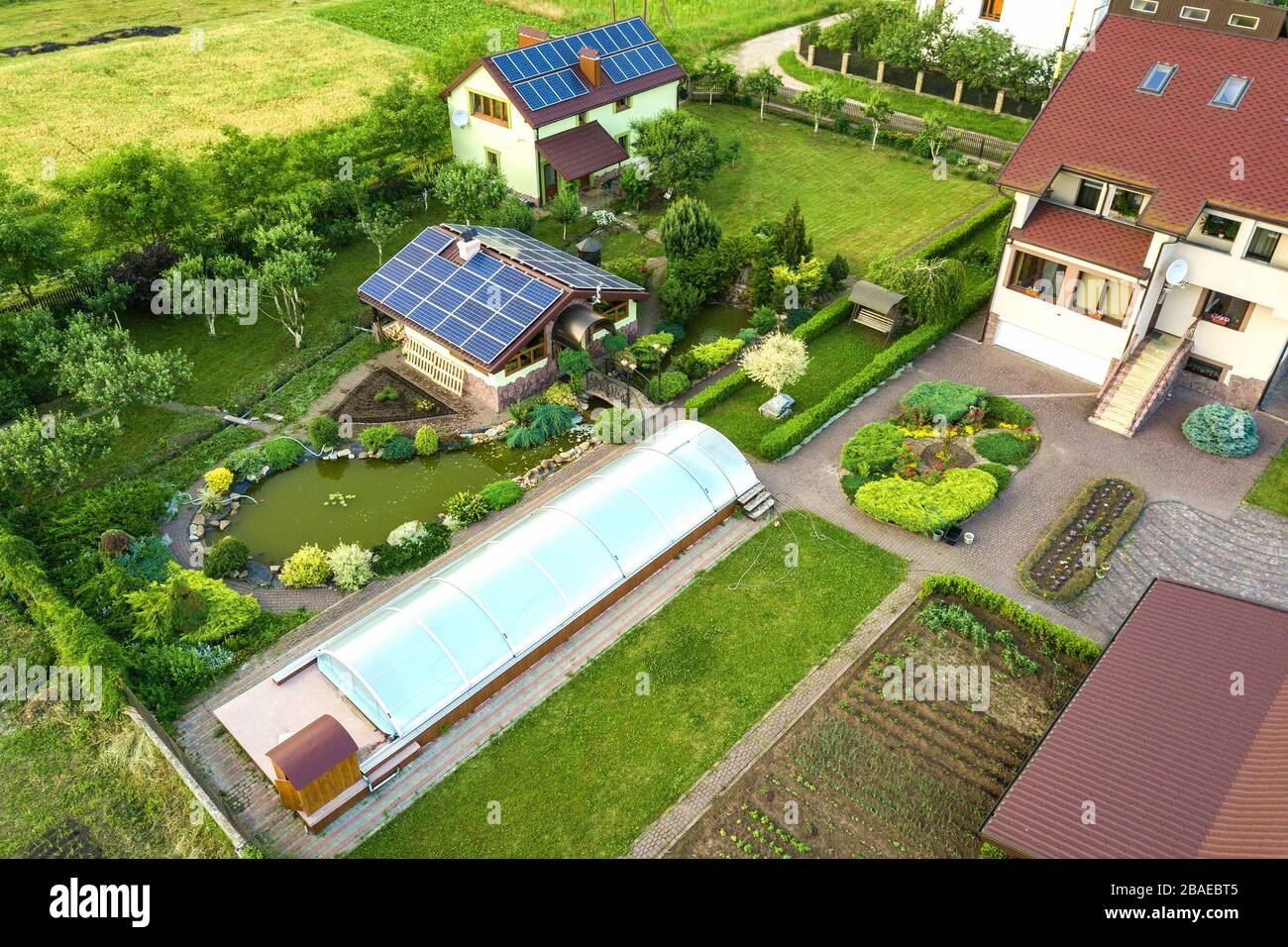 Luftbild eines Privathauses im Sommer mit blauen Sonnenfoto-Voltaikfeldern auf Dach und Grünhof. Stockfoto