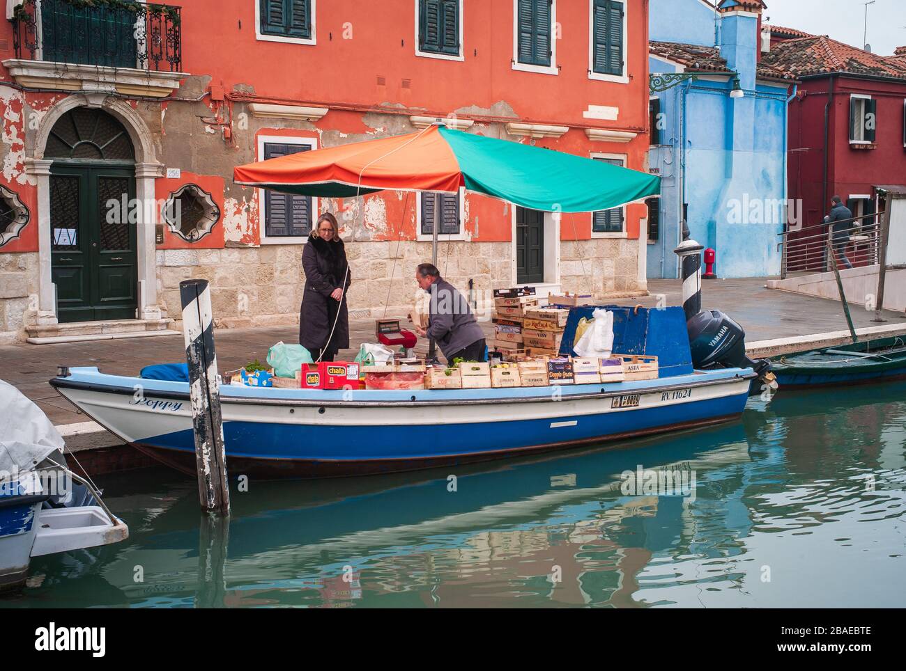 Burano, Venedig, Italien - 3. Januar 2014: Frau kauft Lebensmittel von einem Boot in Venedig. Lebensmittelboote heißen auf Italienisch Barge oder Barca. Stockfoto