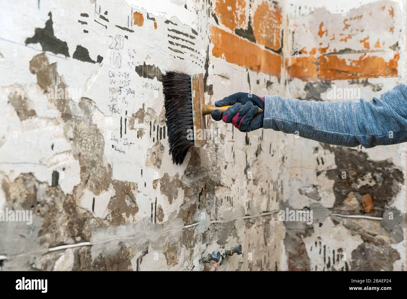 Hand mit Bürste, die Grundierung auf die Wand auftragen, um eine bessere Haftung des Pflasters zu erzielen Stockfoto
