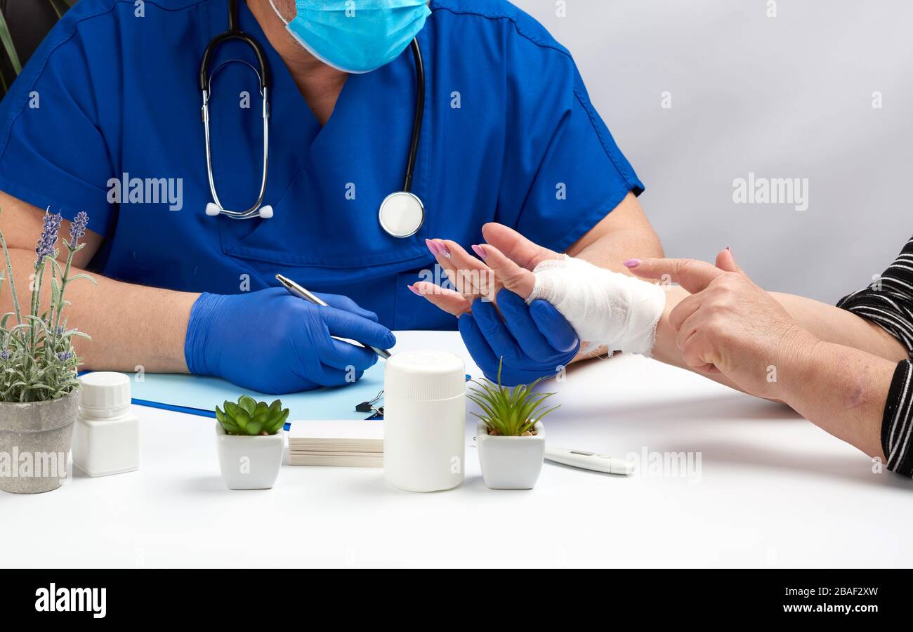 Traumatologe Doktor in blauen Latexhandschuhen sitzt an einem Tisch und hält einen Patientenempfang mit einer Handverletzung, Arztarbeitsplatz Stockfoto