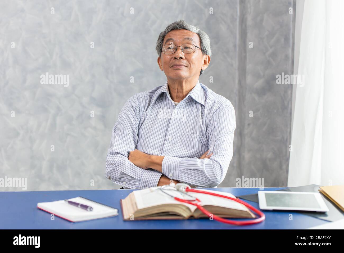 Chinesischer Arzt sitzt am Büroschreibtisch mit Buch Happy Smile gesund stark. Stockfoto