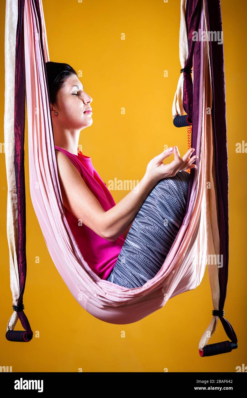 Junge Frau tut Antigravity Yoga meditativen Position im Studio mit gelben Wänden Stockfoto
