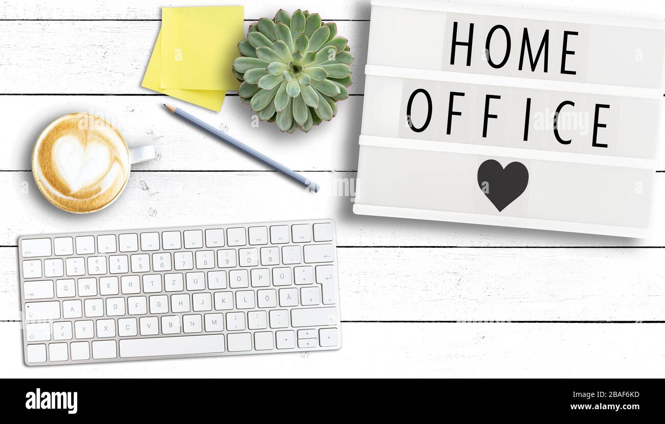 Text HOME OFFICE auf Leuchtkasten auf Holztisch mit Computertastatur, Haftnotizen und Tasse Kaffee, Arbeiten von zu Hause aus während Coronavirus Pandemie Stockfoto