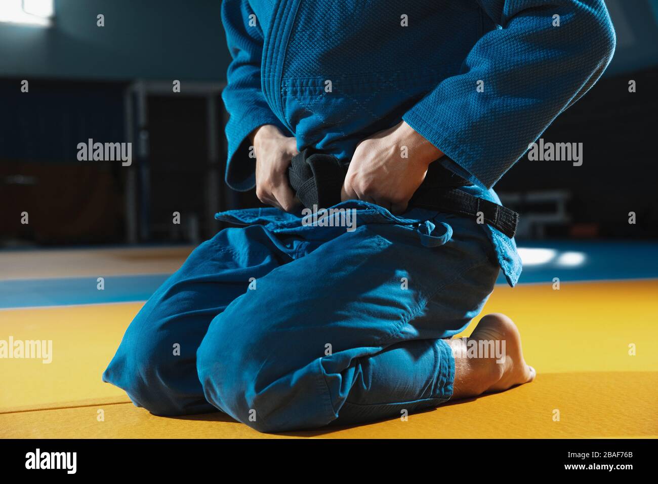 Junger kaukasischer Judo-Kämpfer in blauem Kimono mit schwarzem Gürtel, der in der Sporthalle zuversichtlich ist, stark und gesund. Kampfkünste üben. Überwinden, erreichen des Ziels, Selbstaufbau. Stockfoto