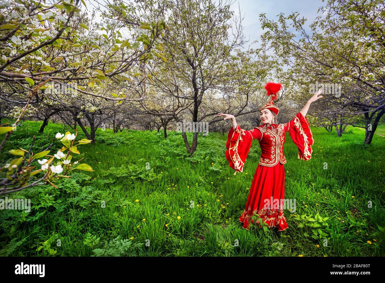 Kasachische Frau tanzt im roten Kleid im Frühjahr blühenden Garten in Almaty, Kasachstan Stockfoto