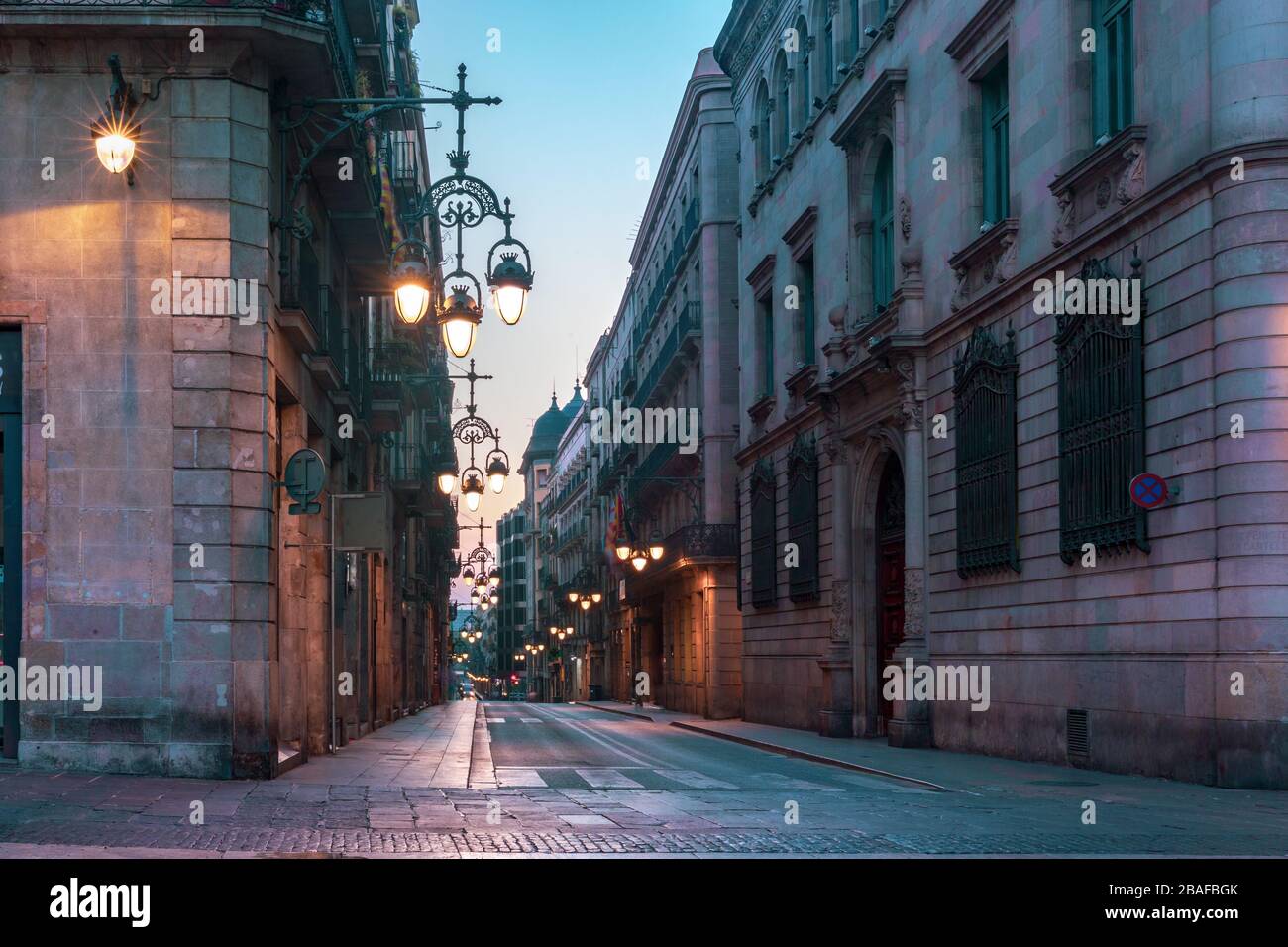 Enge gepflasterte, leere Straße aus dem Mittelalter mit schöner Straßenbeleuchtung im gotischen Viertel Barri am Morgen, Barcelona, Katalonien, Spanien Stockfoto
