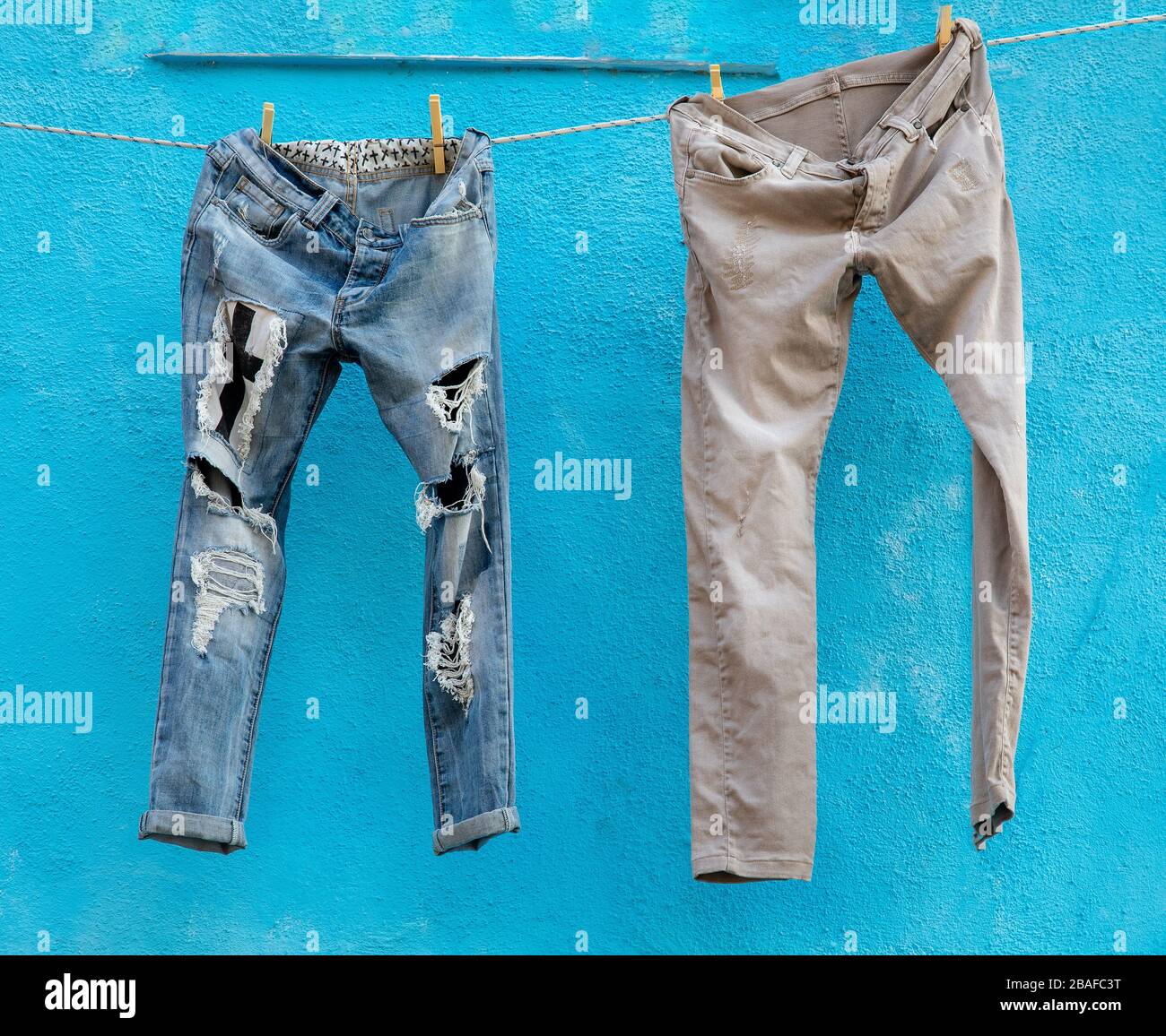 Zwei Paar täterter blauer Jeans, die vor blauem Hintergrund an einer Waschlinie hängen Stockfoto