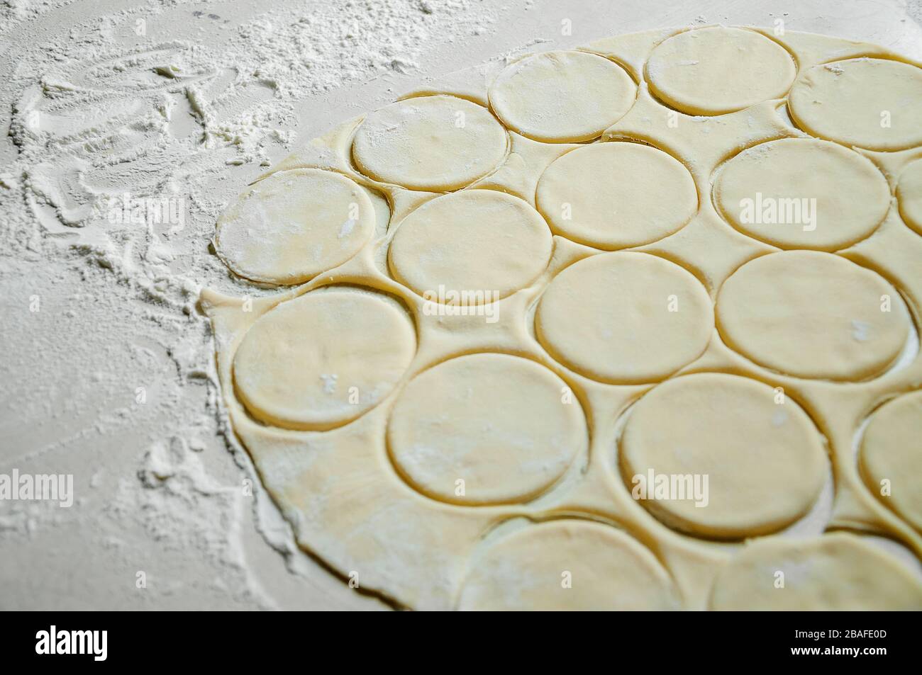Roher ausgerollter Teig, der in Runden mit Mehl auf dem Weißen Tisch geschnitten wurde. Verarbeiten Sie Gardudeln. Stockfoto