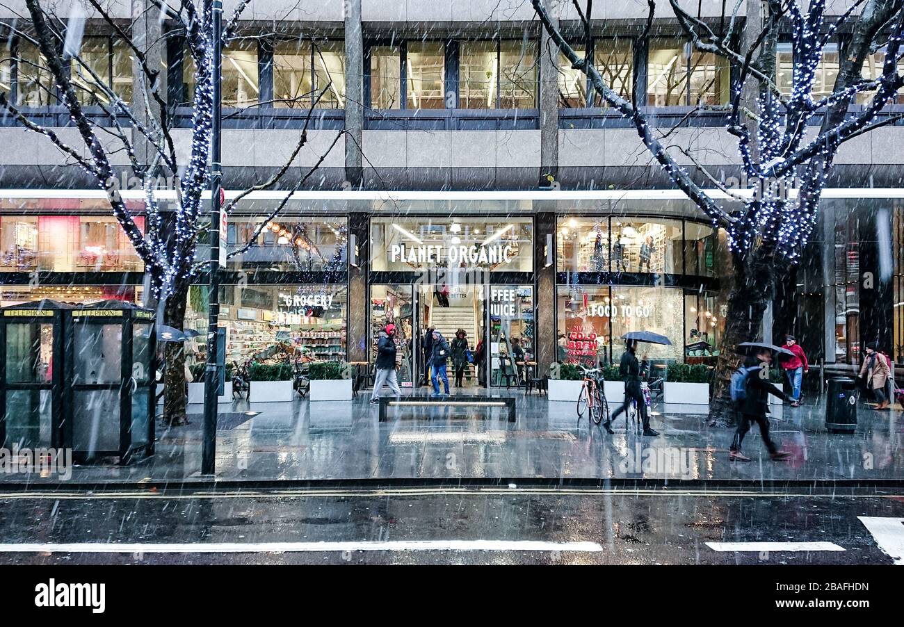 Planet Organic. Eine geschäftige Londoner Straßenszene mit Weihnachtskäufern auf der Tottenham Court Road an einem kalten und schneien Wintertag. Stockfoto