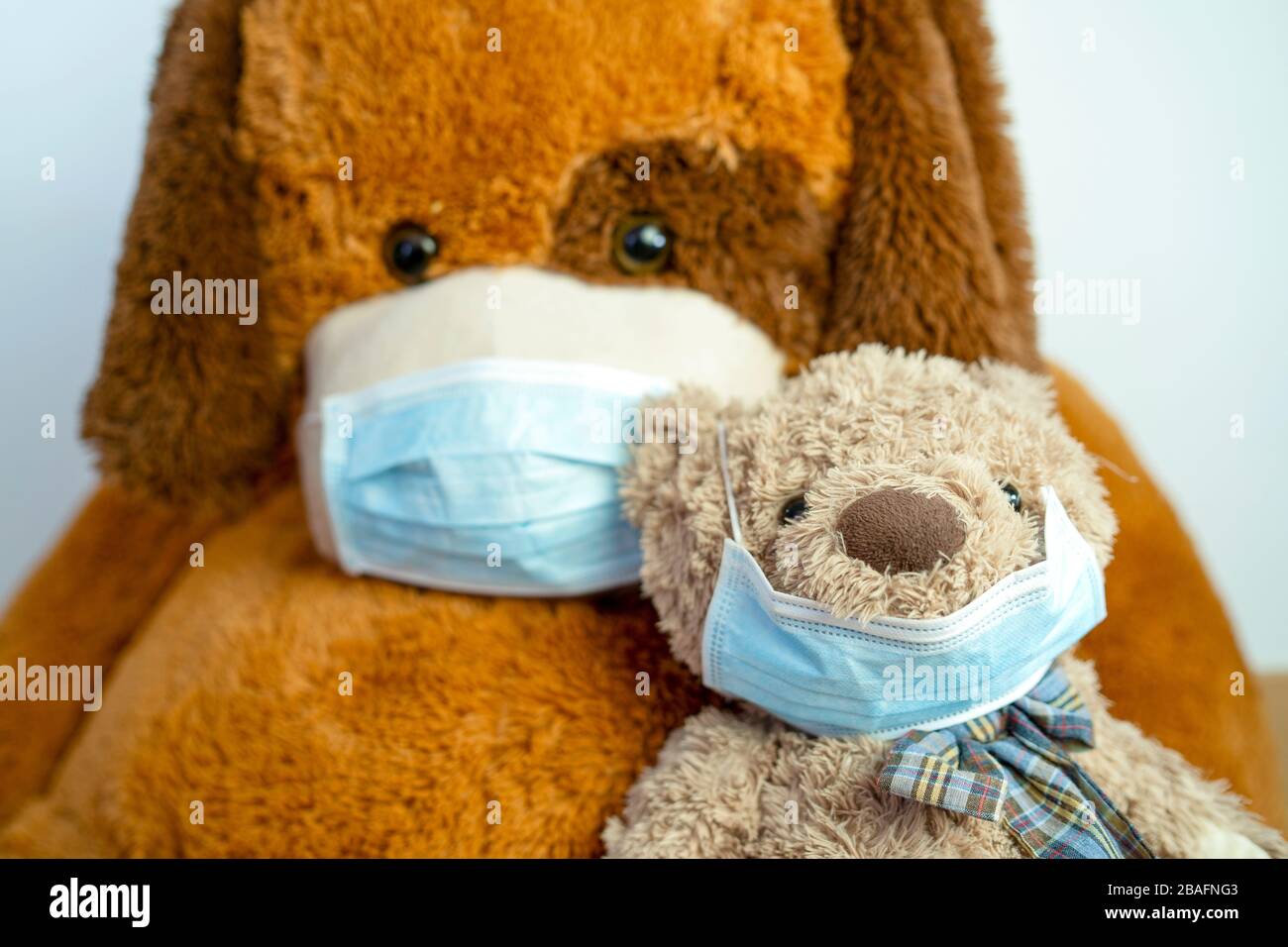 Zwei braune Teddybären - klein und groß - tragen aus gesunden Gründen blaue Schutzmasken Stockfoto