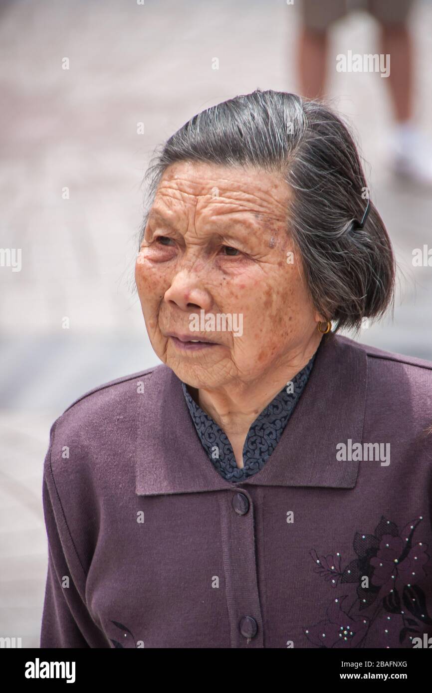 Shanghai, China - 4. Mai 2010: Nahaufnahme des Gesichts der älteren, grauenden, in violettem Gewand gekleideten Seniorin. Stockfoto