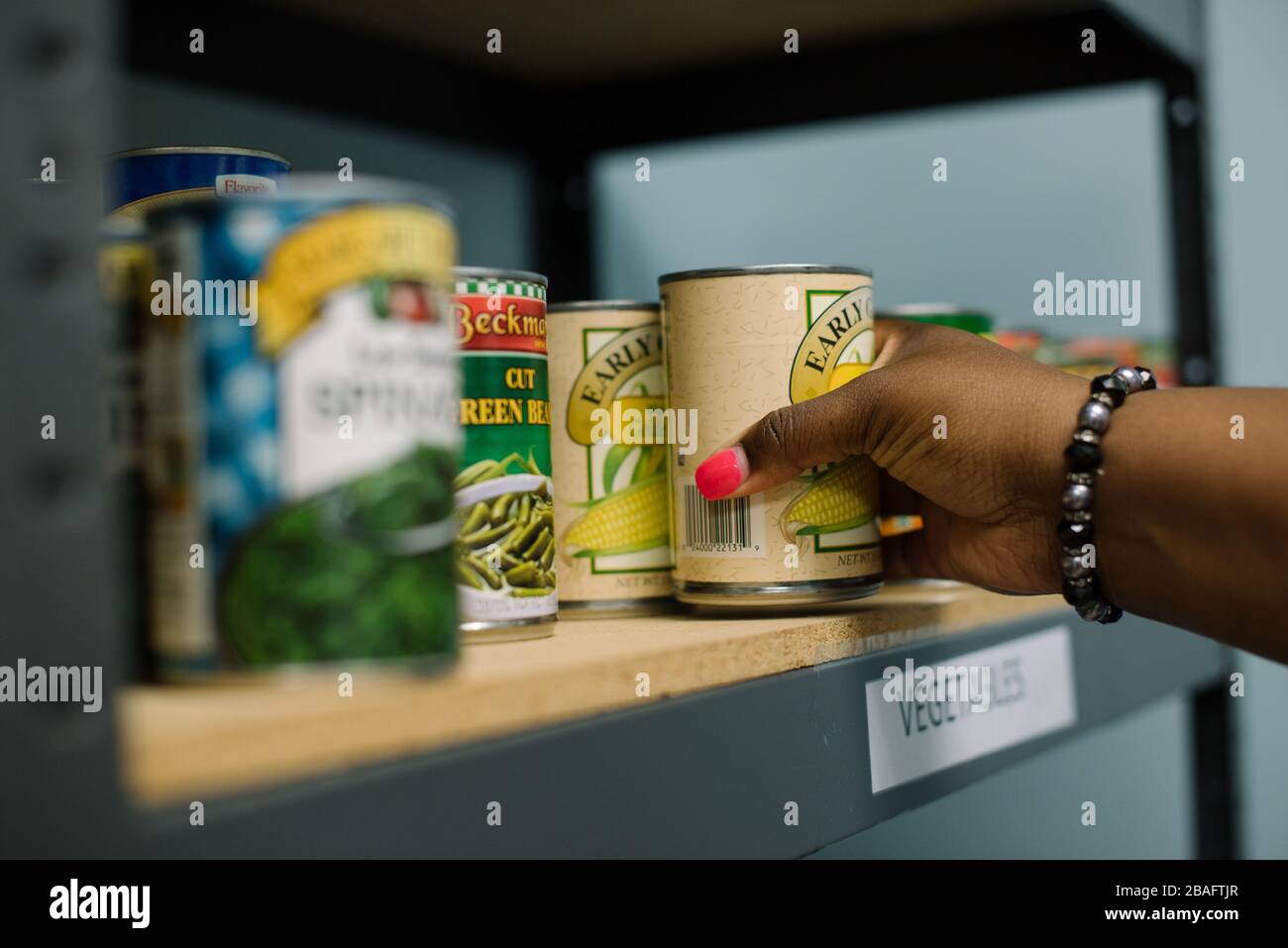 Die Hand der schwarzen Frau, die bei einem nach einer Dose Nahrung greift Speisekammer Stockfoto