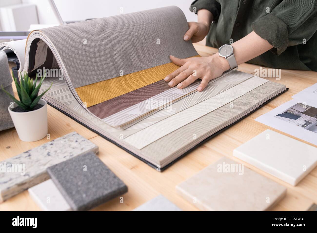 Die Hände des jungen Designers des Innenraums, der am Tisch steht und die Tapeten für eine neue Bestellung unter den Plattenproben wählt Stockfoto