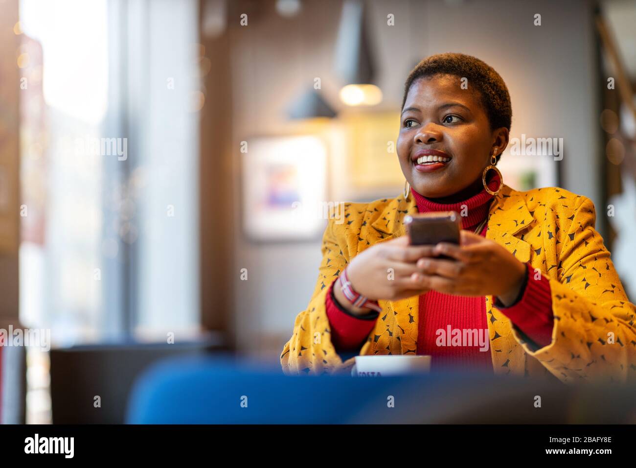 Fröhliche junge Frau mit Smartphone in einem Café Stockfoto