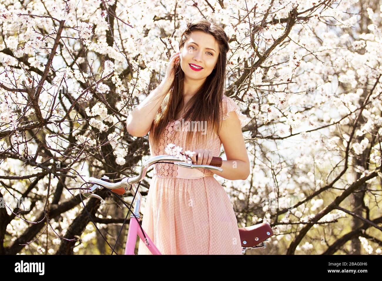 Schönheitsportrait zart, attraktives und junges langhaariges Mädchen in rosafarbenem Kleid, das mit Retro-Rad auf Blumenhintergrund steht. Stockfoto