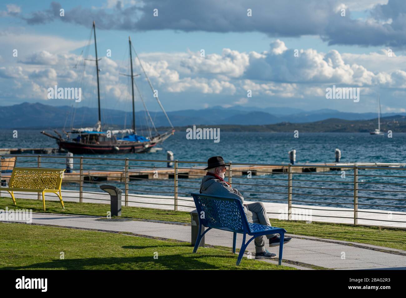 Sardinien; Italien; EIN Senior sitzt auf einer Holzbank am Meer und entspannt sich Stockfoto