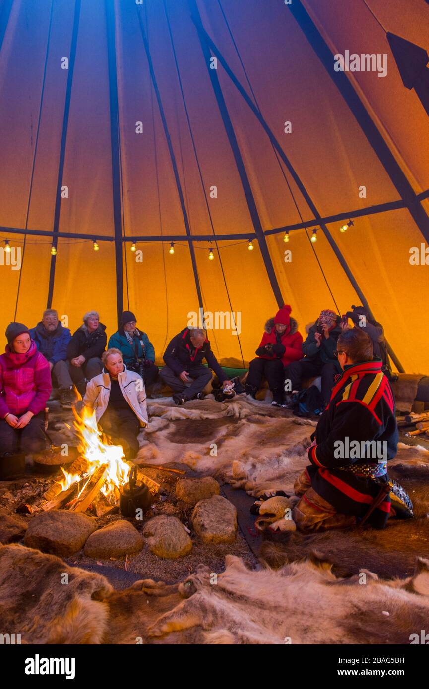 Touristen in einem Lavvu, einem Zelt, das eine temporäre Wohnung ist, die von den samischen Leuten hier im samischen Dorf Ravttas bei Kiruna im schwedischen Lapla benutzt wird Stockfoto