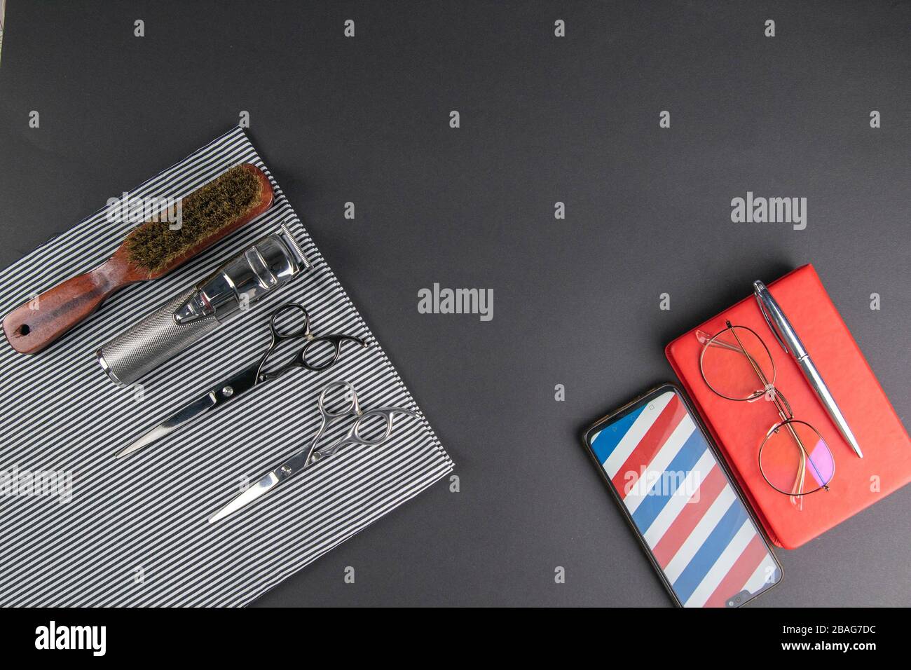 Eine Maschine für Haarschnitte, Schere, Kammständer auf einem weißen Handtuch und neben dem Telefon gibt es einen Stift und ein rotes Notizbuch, auf dem sich eine Frauenbrille befindet Stockfoto
