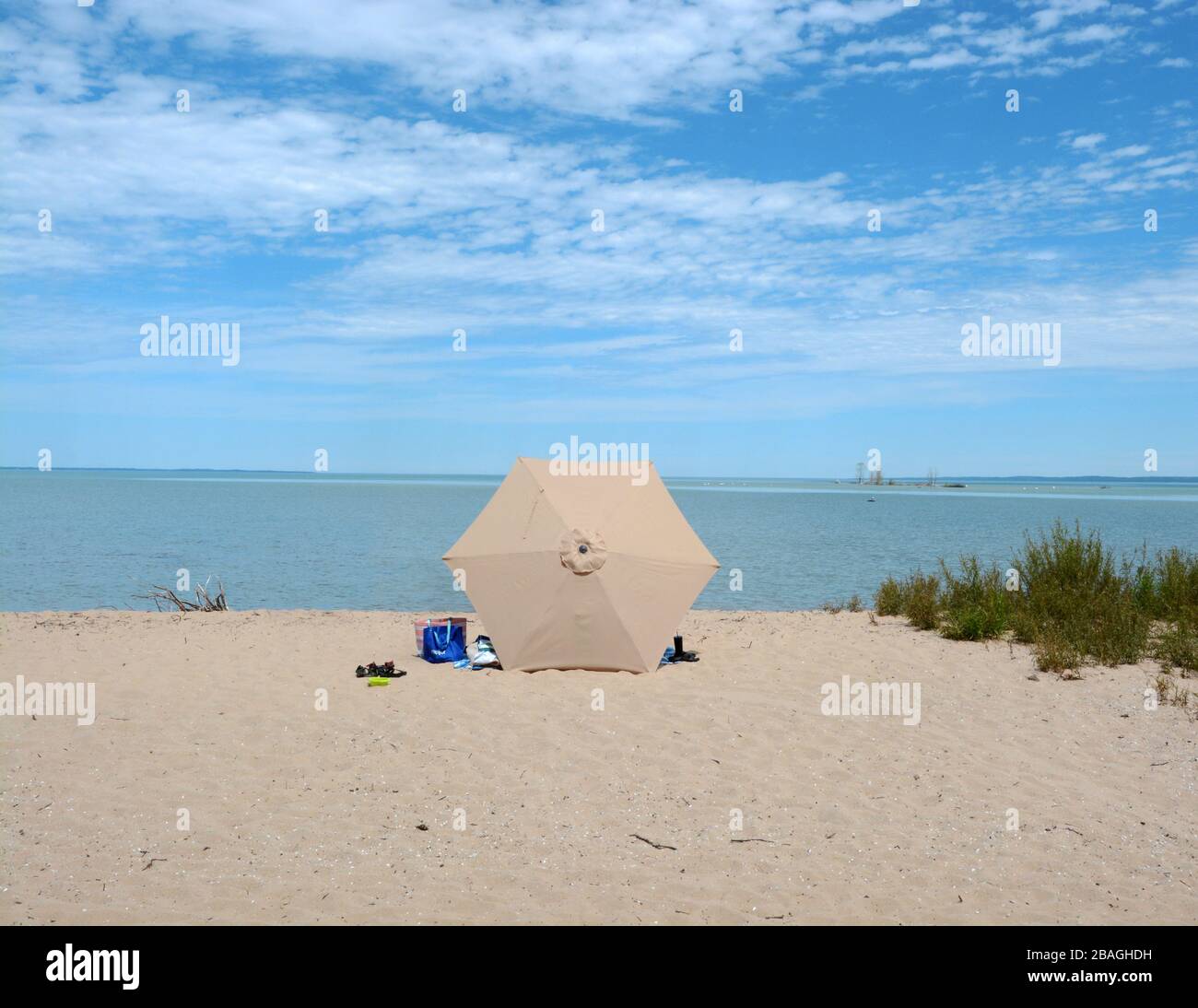 Ein brauner Regenschirm an einem braunen sandigen Strand mit blauem Wasser und Himmel im Hintergrund. Stockfoto