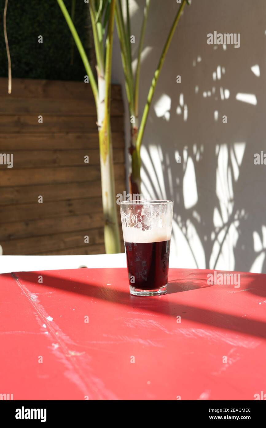 Ein halbes Pint Guinness auf einem Tisch draußen in der Sonne. Stockfoto