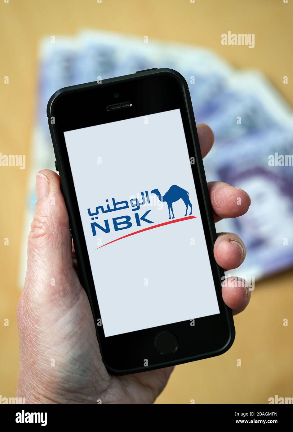 Eine Frau, die auf einem Handy das Logo der NBK National Bank of Kuwait betrachtet. (Nur redaktionelle Verwendung) Stockfoto