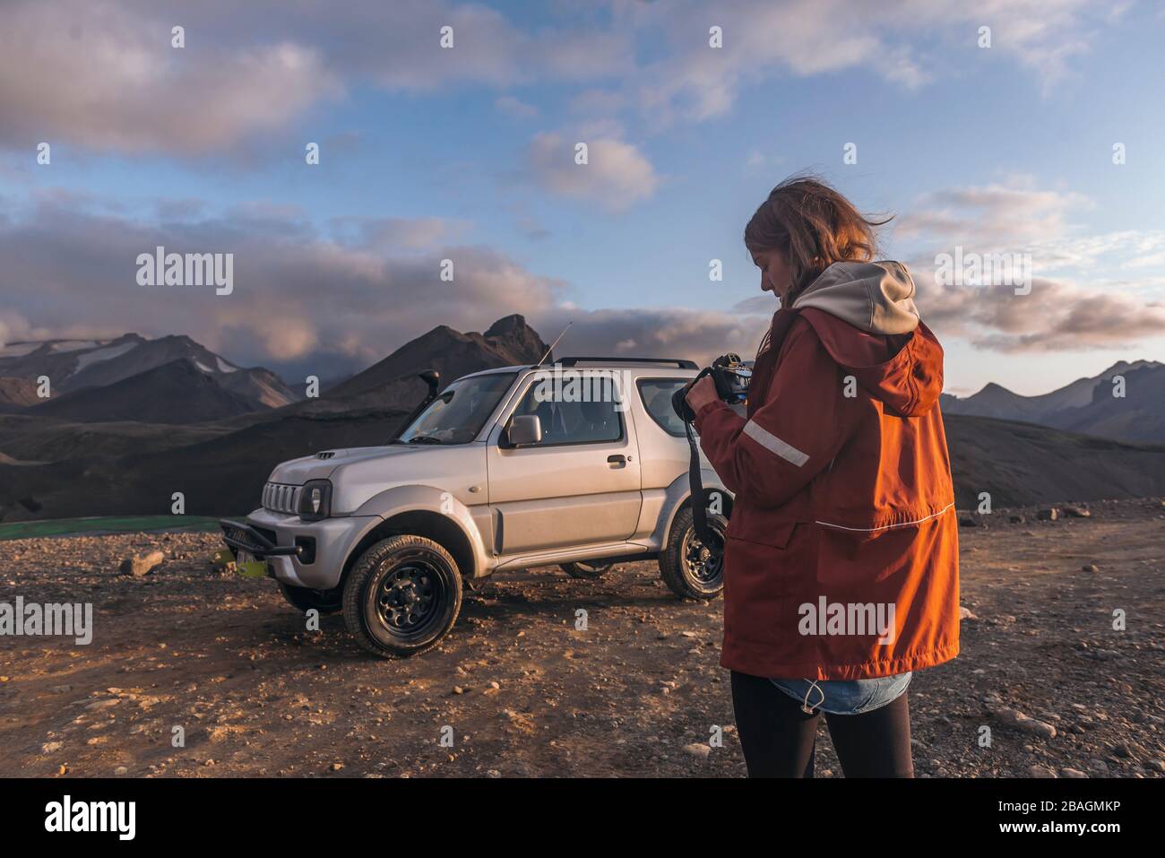 Junge Frau, die vor dem Auto in den Bergen auf die Kamera schaut Stockfoto