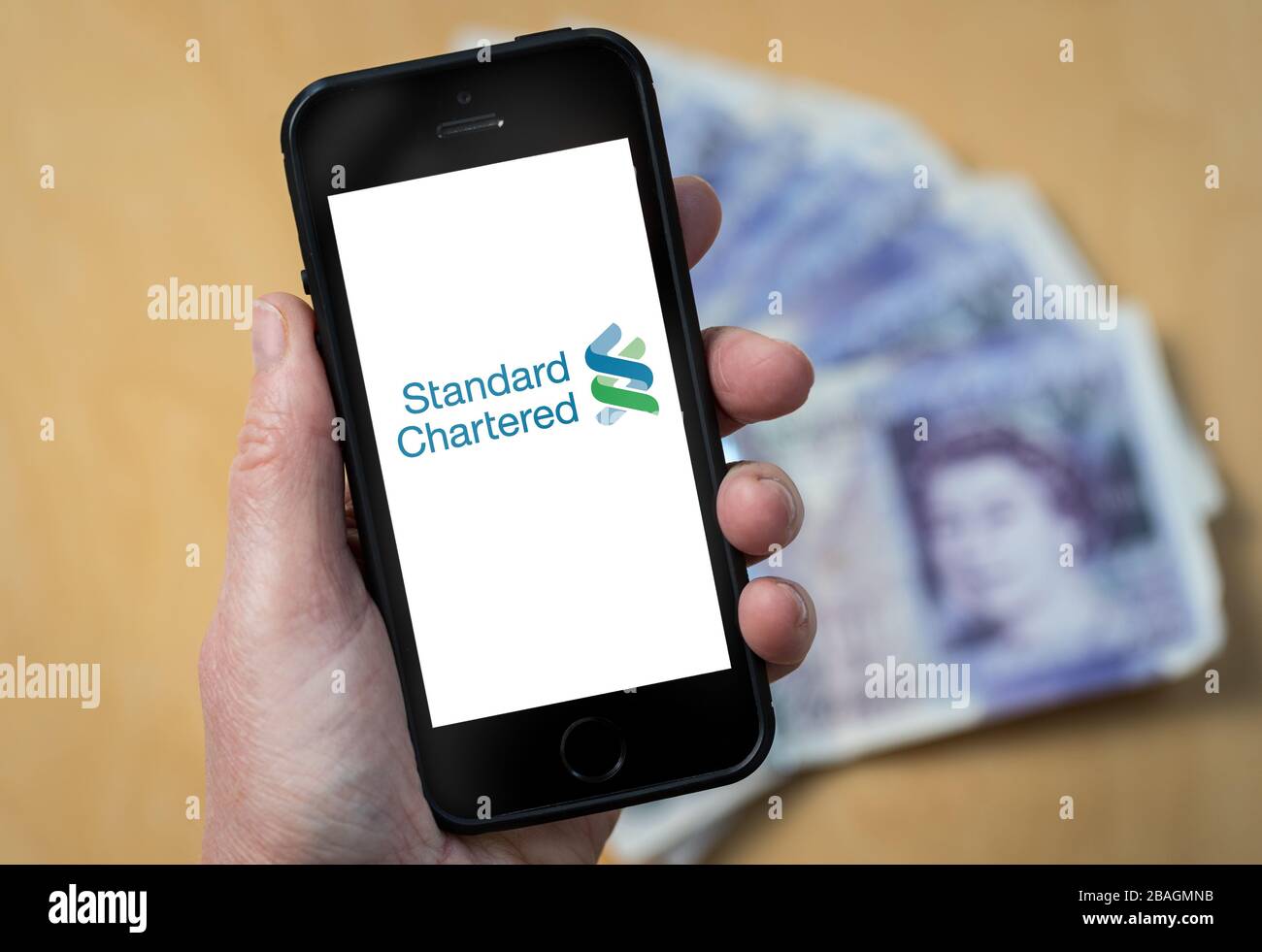 Eine Frau, die das Logo der Standard Chartered Bank auf einem Mobiltelefon betrachtet. (Nur redaktionelle Verwendung) Stockfoto