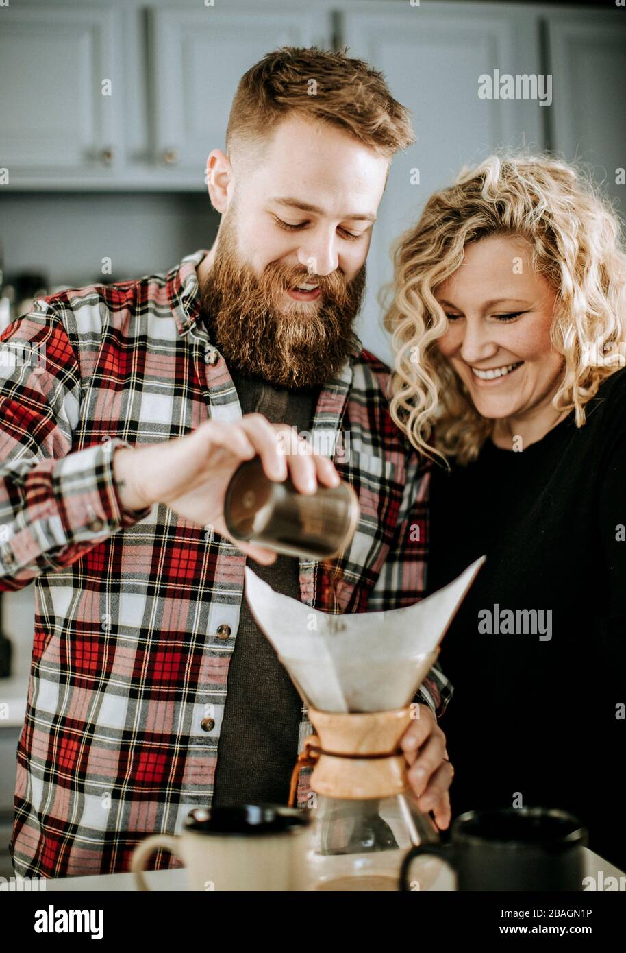Mann und Frau lächeln, während sie sich darauf vorbereiten, einen Kaffee zu übergießen Stockfoto