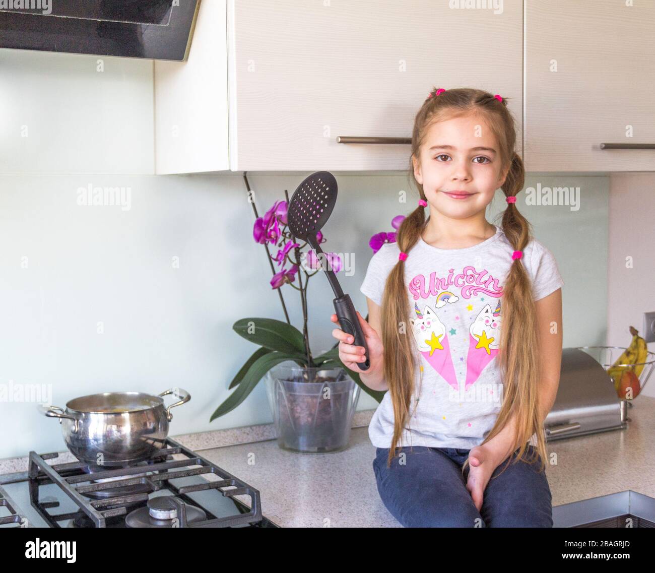 Kleines Mädchen, das in der Küche sitzt und sich zum Kochen vorbereitet. Quarantänekonzept für Coronavirus. Bleiben Sie zu Hause. Stockfoto