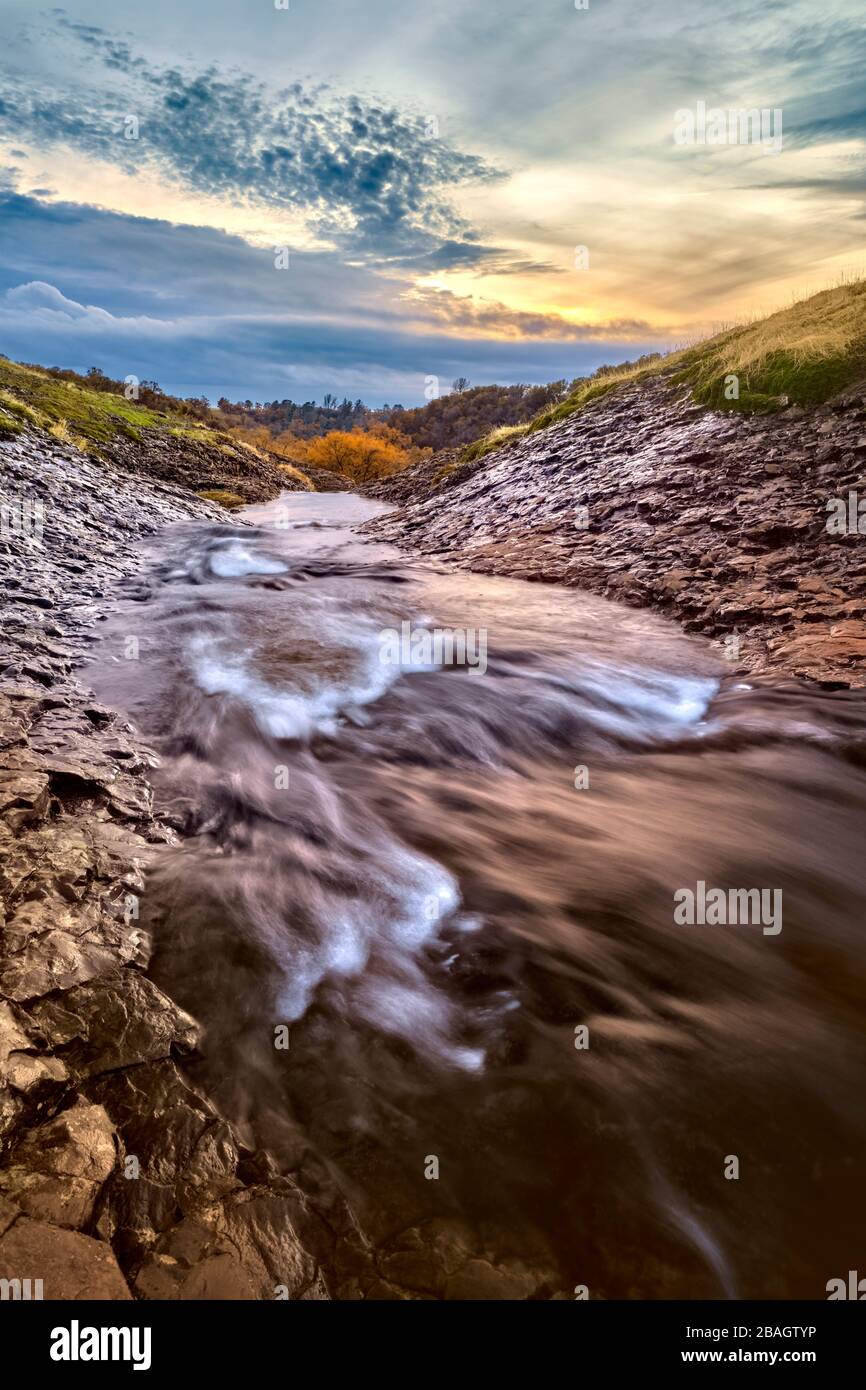 Lange Exposition des Mountain Creek, der bei Sonnenuntergang durch ein grünes Rasenfeld läuft. Stockfoto