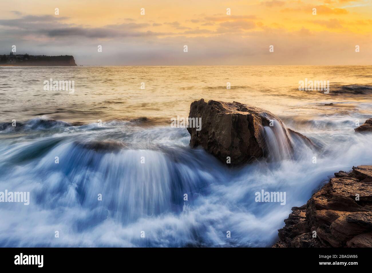 Großer Felsbrocken, der bei Sonnenaufgang an den Nordstränden von Sydney von großer Meereswelle überrollt wurde. Stockfoto