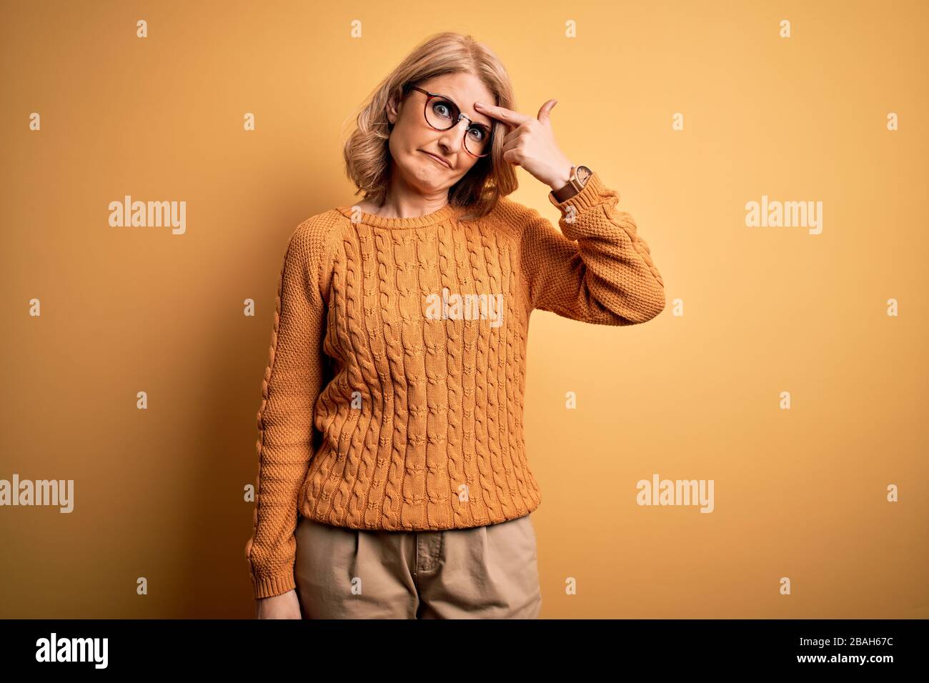 Mittlere Zeit schöne blonde Frau mit legeren Pullover und Brille über gelbem Hintergrund, die unglücklich auf den Zuhälter auf der Stirn zeigt, hässliche Infektion von Stockfoto