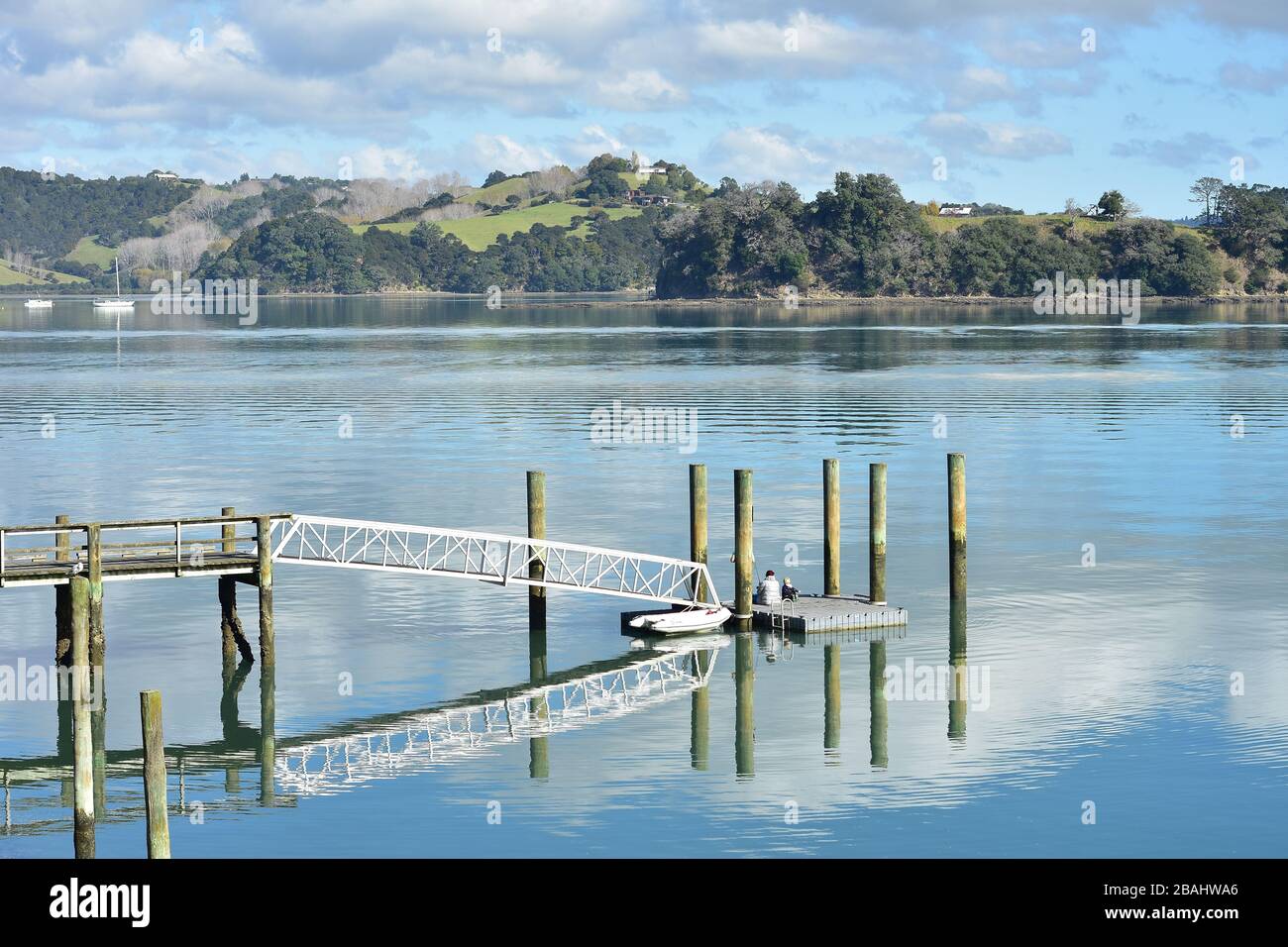 Winziger schwimmender Steg auf dicken Holzpfosten, der am sonnigen Tag im ruhigen Spiegelhafen reflektiert wird. Stockfoto