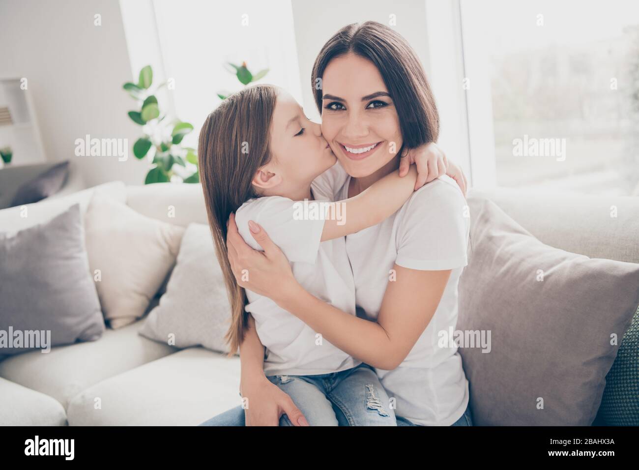 Portrait der positiven fröhlichen süßen Mama und ihres kleinen Mädchens  Kiss Mama Kuschelarme genießen Sie die freie Zeit zusammen verbringen Divan  im hellen Raum Stockfotografie - Alamy