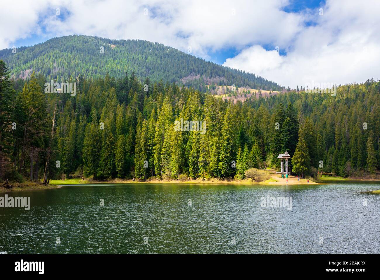 alpiner Bergsee im Wald. Schönes, sonniges Wetter mit flauschigen Wolken am blauen Himmel. Frühlingsszenerie in dappeltem Licht. Gewässer Stockfoto