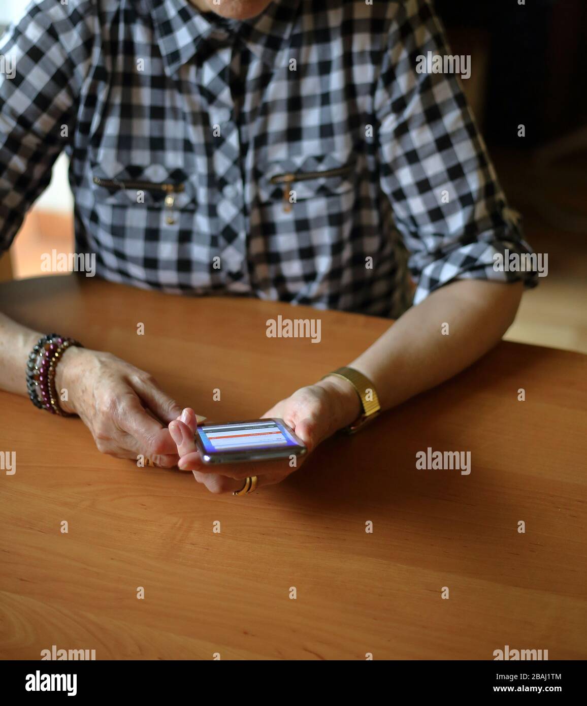 Seniorin Frau sitzt einsam am Holztisch mit Smartphone, um zu kommunizieren. Stockfoto