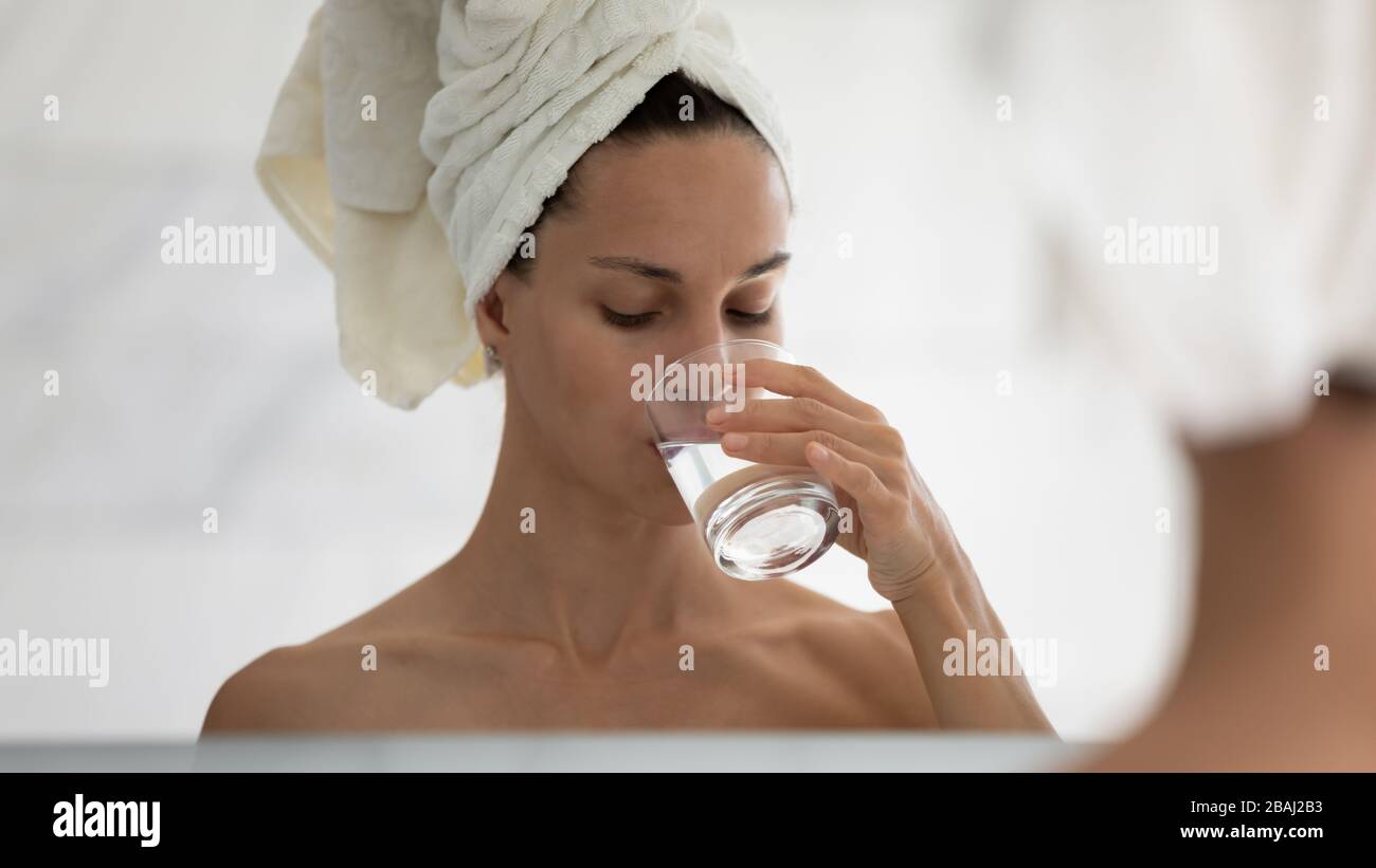 Frau schlug sich im Spiegel nieder, während sie stilles Wasser trinkt Stockfoto