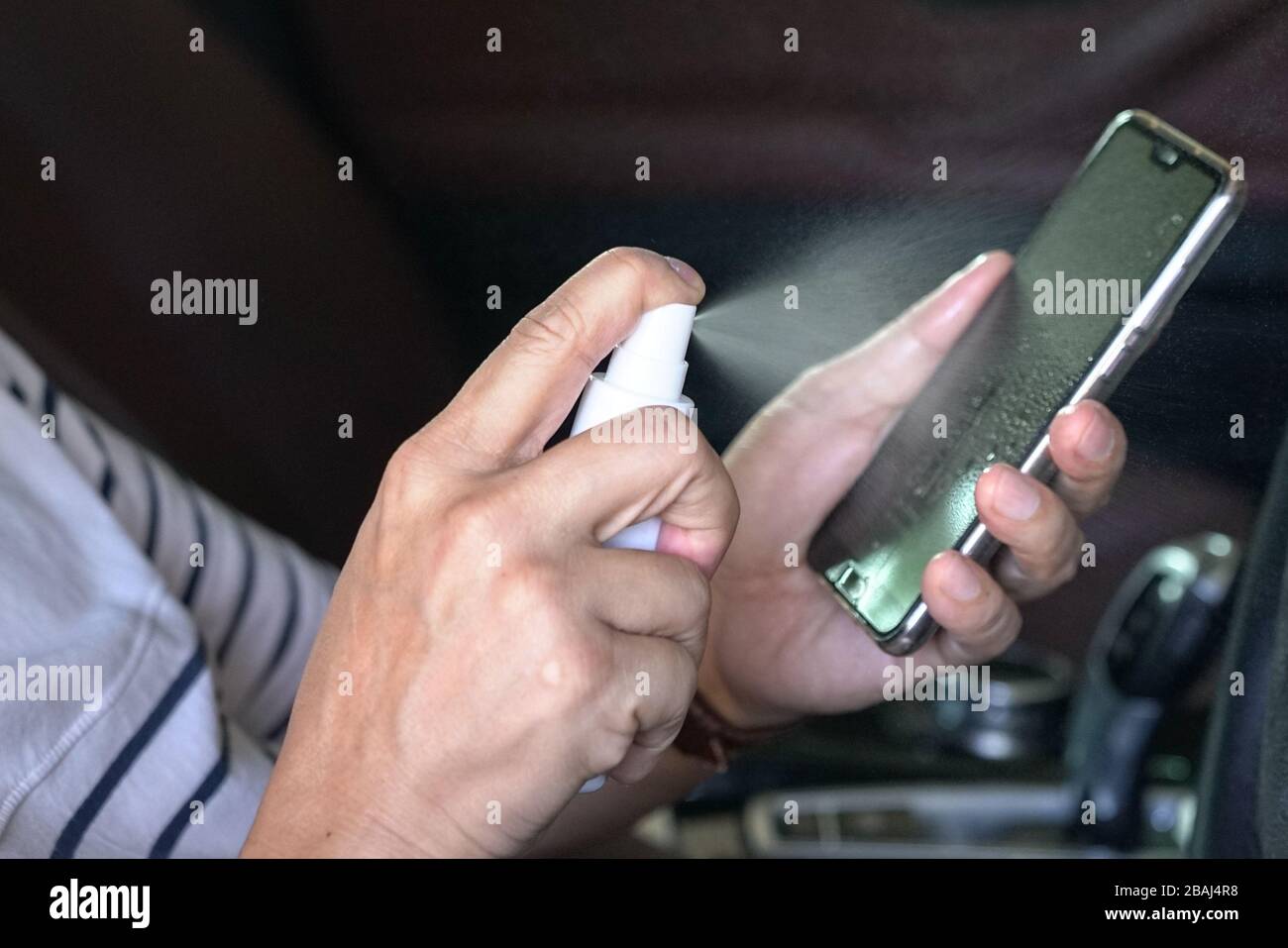 Man sprüht Desinfektionsmittel auf sein Handy. Bleiben Sie gesund, oder töten Sie Viren oder Bakterien. Stockfoto