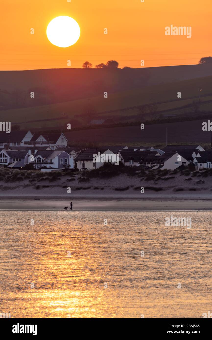 Instow, North Devon, England. Samstag, 28. März 2020. Ein heller, aber kühler Start in den Tag in Nord-Devon. Im krassen Gegensatz zum Vorwochenende hat bei Sonnenaufgang ein einsamer Hundewanderer den Strand bei Instow für sich, als eine neue Richtlinie, die Menschen auffordert, nicht zu fahren, um ihre Hunde auszuüben, zu den sozialen Distanzierungs- und Selbstisolierungsmaßnahmen hinzukommt, um die Ausbreitung von Covid-19 zu begrenzen. Kredit: Terry Mathews/Alamy Live News Stockfoto