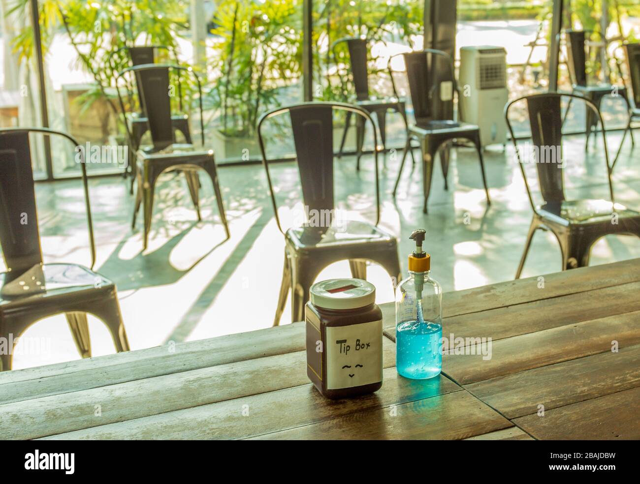 Soziale Distanzierung, Alkoholgel und Trinkbox auf Tisch mit leeren Stühlen. Stockfoto