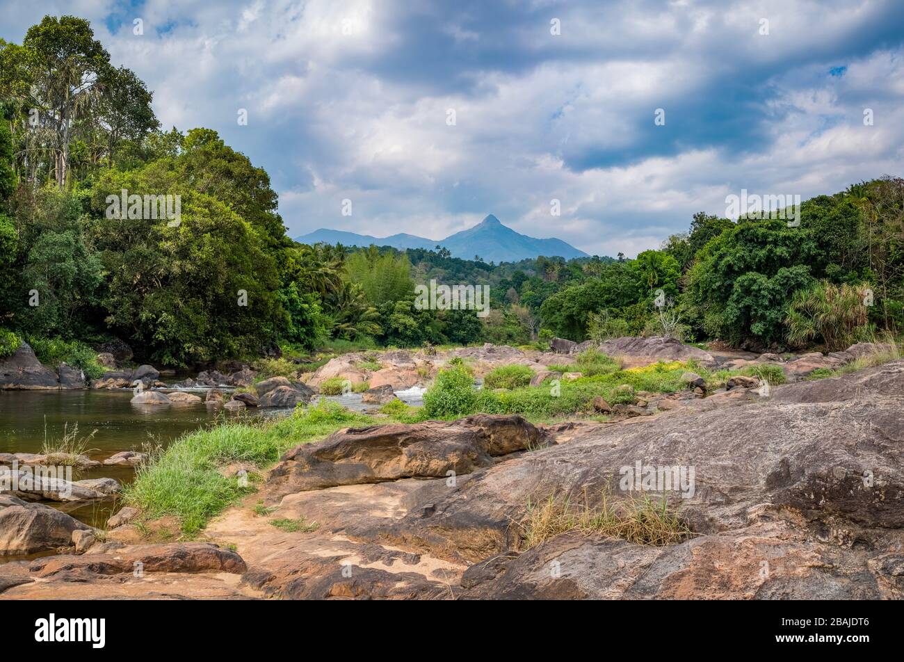 Blick auf einen felsigen Fluss und einen Berggipfel. Während eines teilweise übergiebelten Frühlingsnachmittags in der Nähe von Munnar, Kerala, Indien eingenommen. Stockfoto