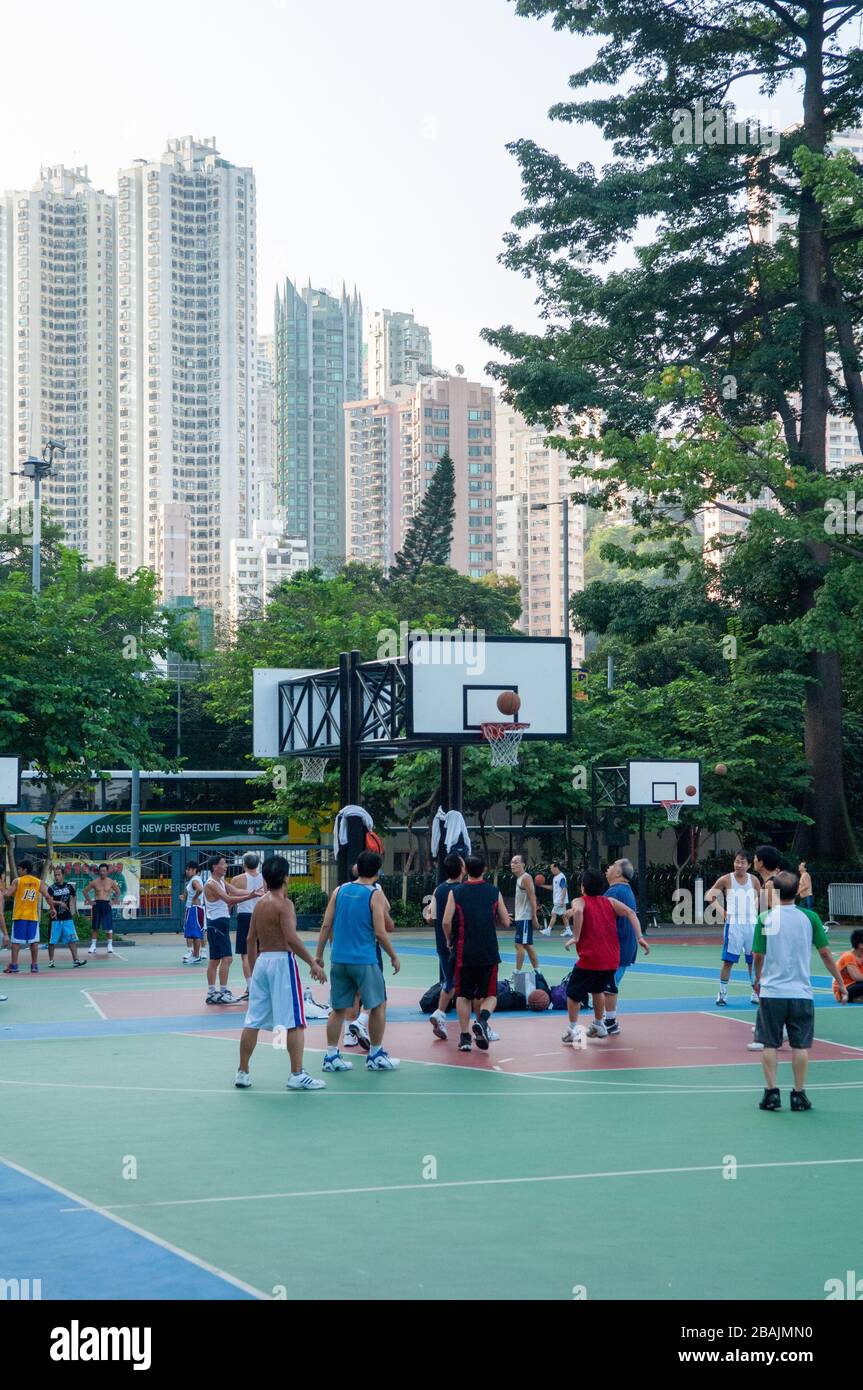 Junge Männer, die im Victoria Park, Hongkong, auf einem Allwetterboden trainieren und Basketball spielen. Mit hohen Gebäuden, die den Hintergrund bilden. Stockfoto