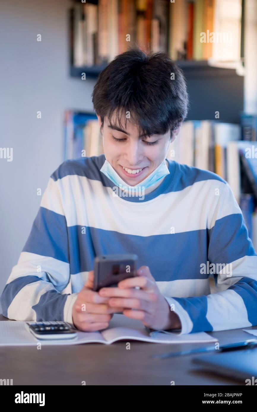 Ein Student der Hochschule trägt eine Maske und nimmt sich Zeit aus seinem Studium, um auf seinem Handy zu zeigen Stockfoto