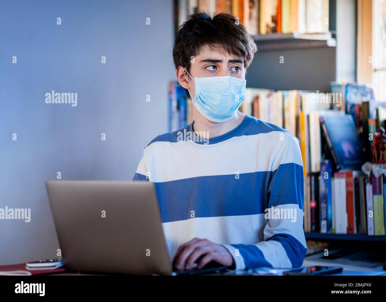 Ein Teenager, der zu Hause eine Schutzmaske trägt, die auf dem Schoß studiert Stockfoto