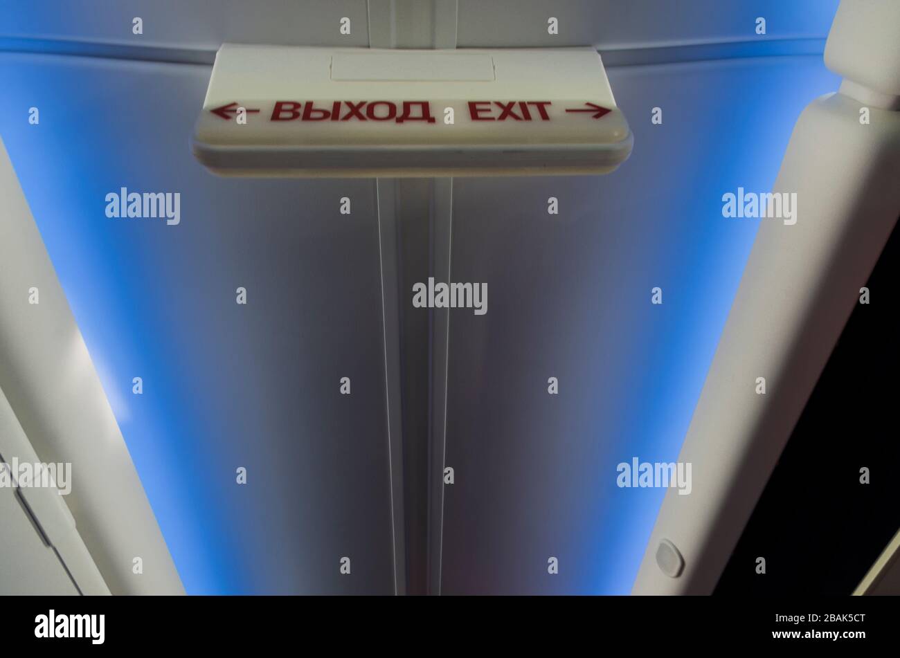 Leuchtendes Schild "Ausgang" in Russisch und Englisch im Flugzeug hoch über dem Kopf auf blauem Hintergrund mit Beleuchtung Stockfoto