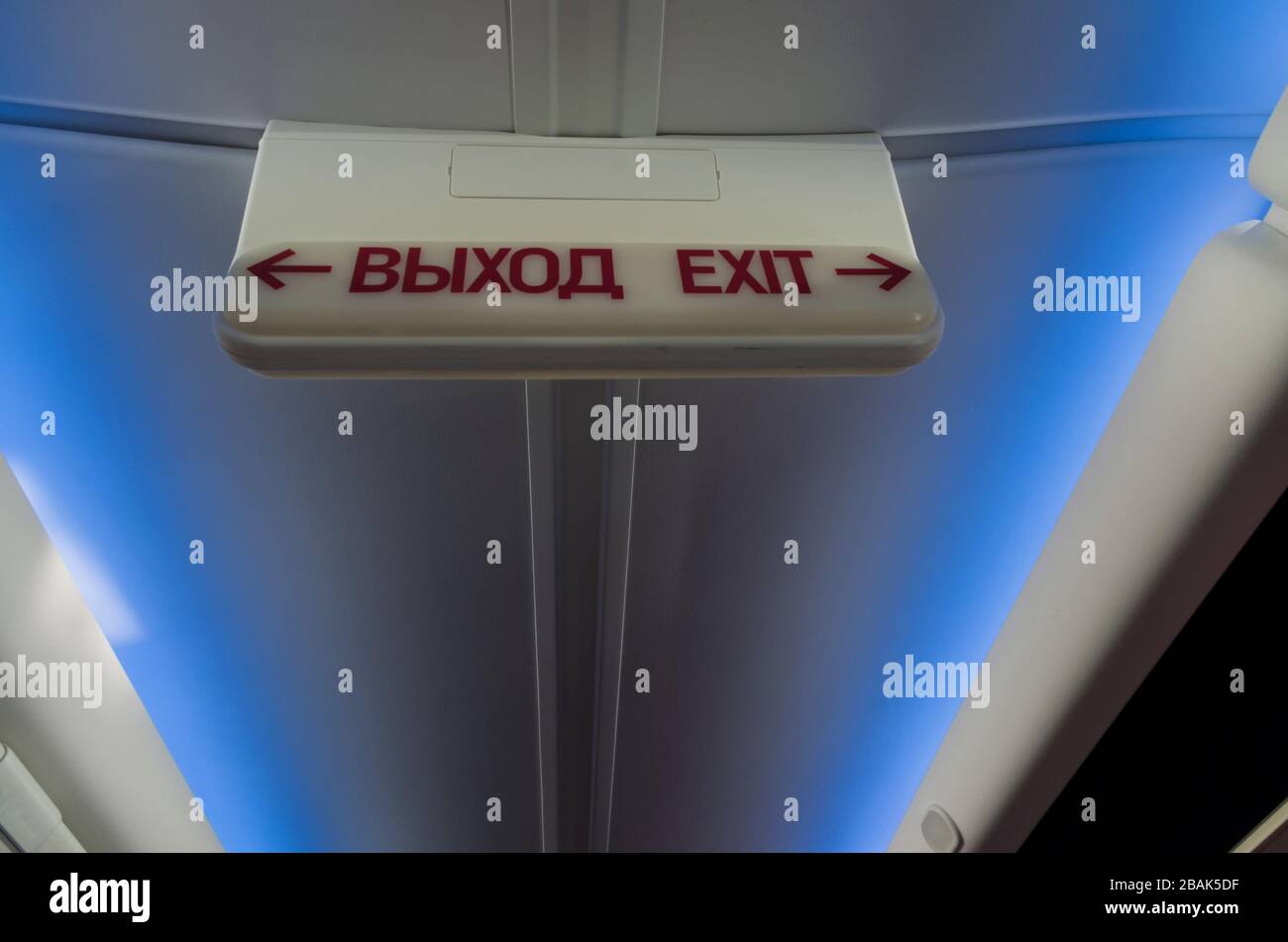 Informationen Lichtschild "Ausgang" in Russisch und Englisch im Flugzeug auf dem Hintergrund der Decke mit blauem Licht Stockfoto