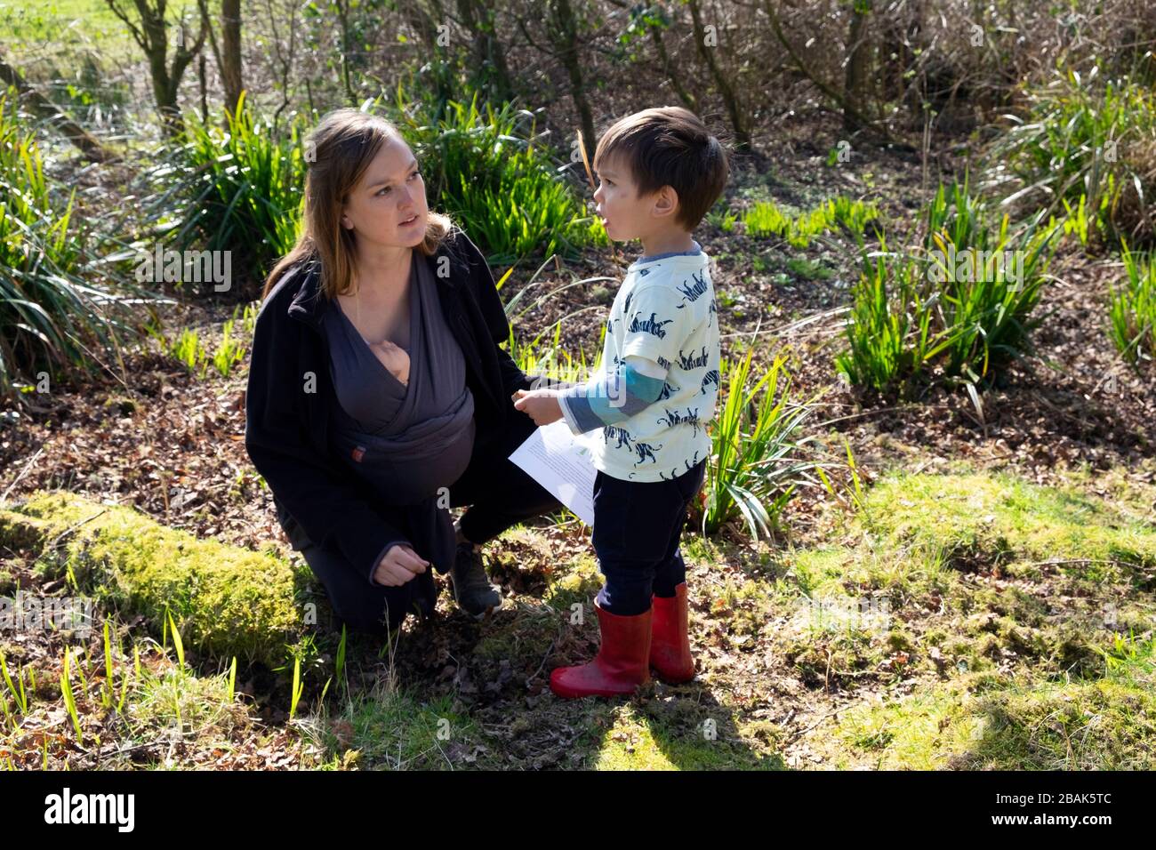 Eine Mutter, ein kleines Kind und ein Baby in einem Stoffschlingenträger während des Coronavirus Outbreak 2020, das eine Naturlehrbuchaktivität zu Hause in Wales UK 2020 macht Stockfoto