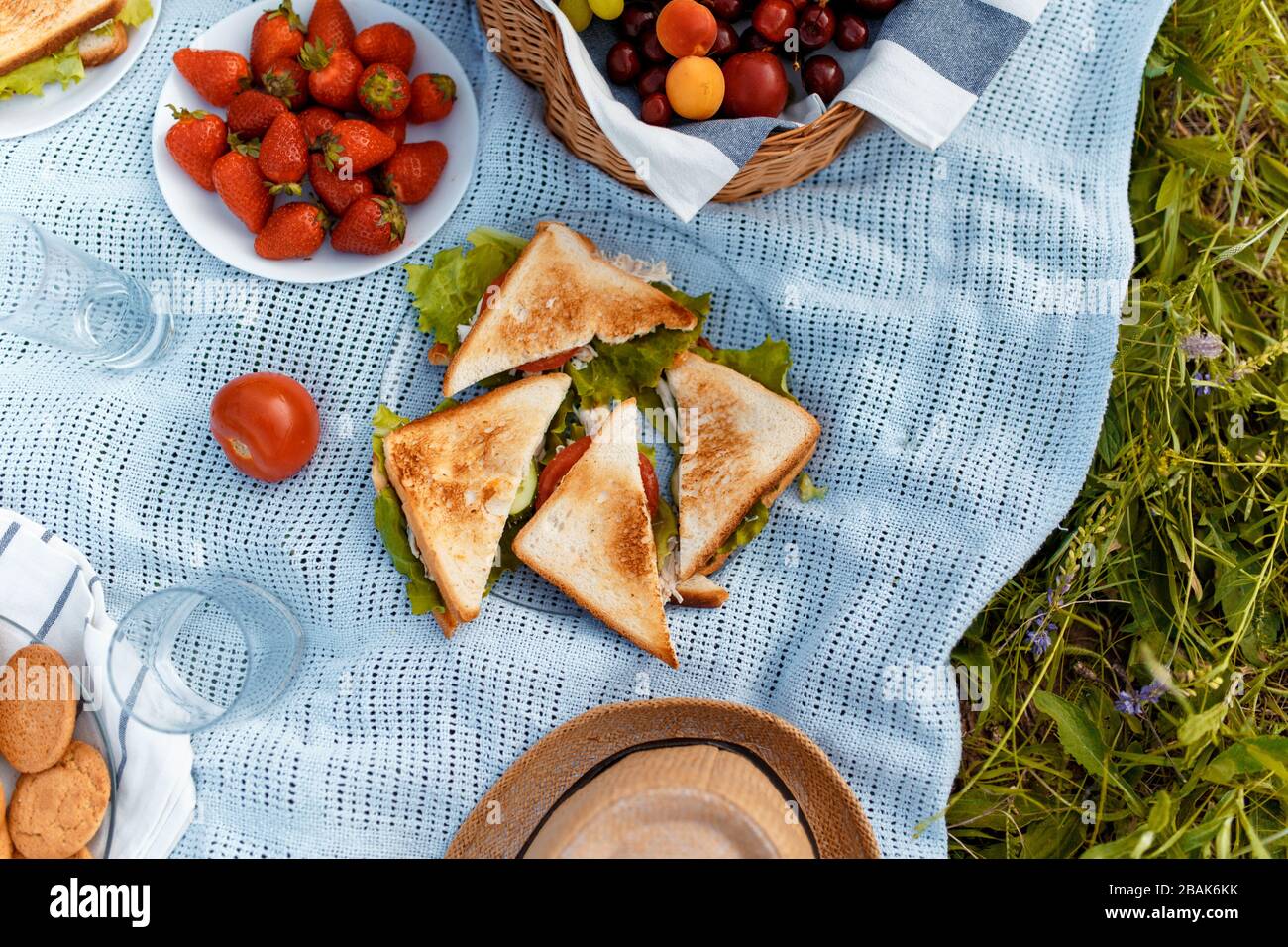 Sommerpicknick auf dem Gras mit einem offenen Picknickkorb, Obst, mit getoasteten Sandwiches und Beeren. Picknicktablectloth. Blick von oben. Stockfoto