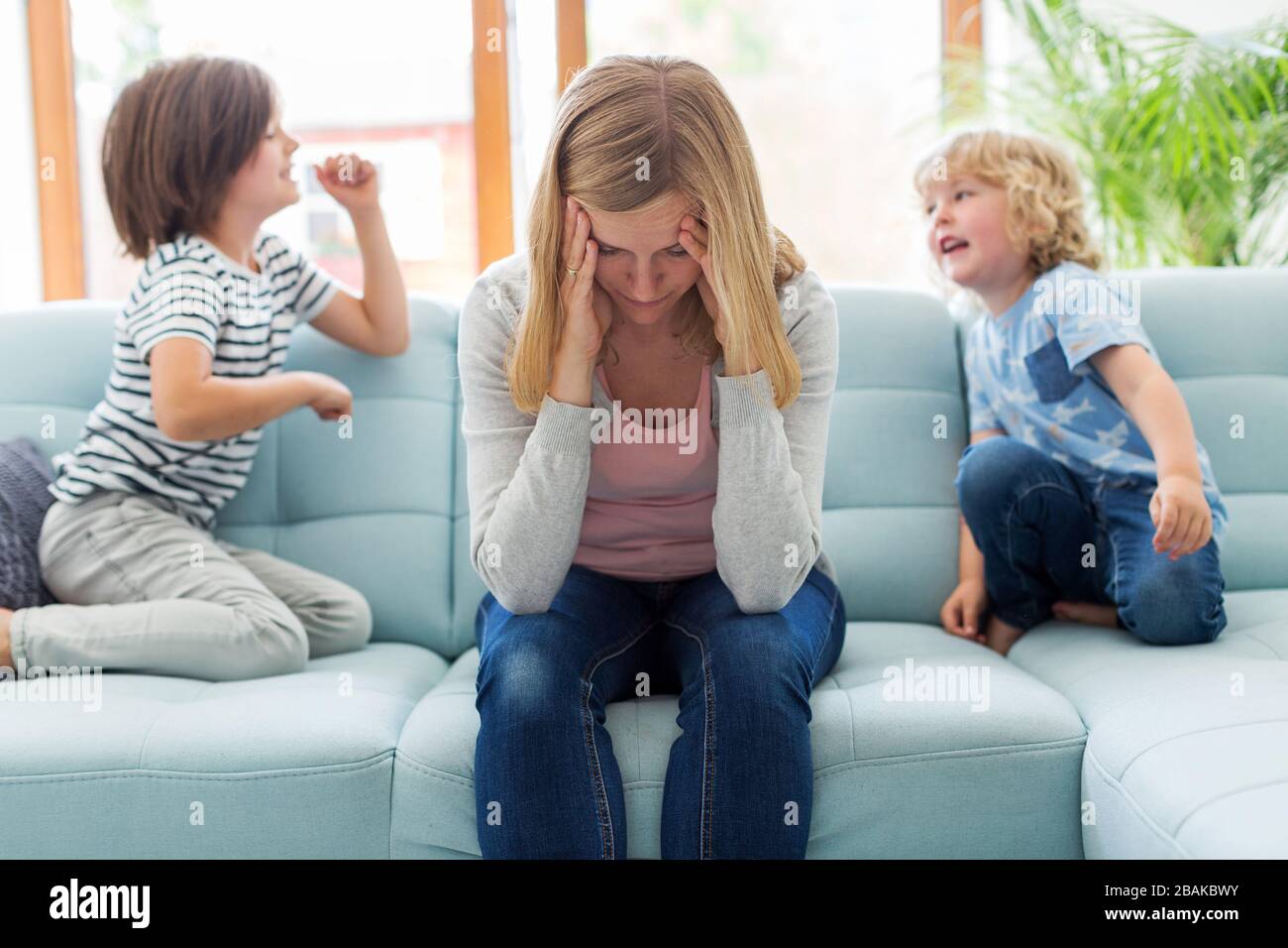 Mutter mit Kopfschmerzen und Kinder springen auf dem Sofa Stockfoto